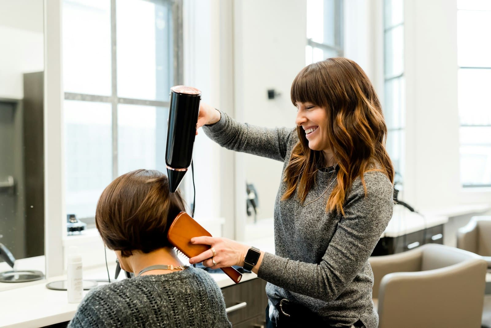Hair stylist blow-drying a client's hair in a bright salon